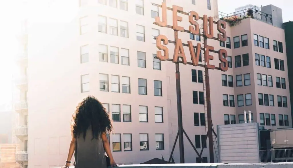 Woman looking at "Jesus Saves" sign on city building, exploring Christian faith and doubts.