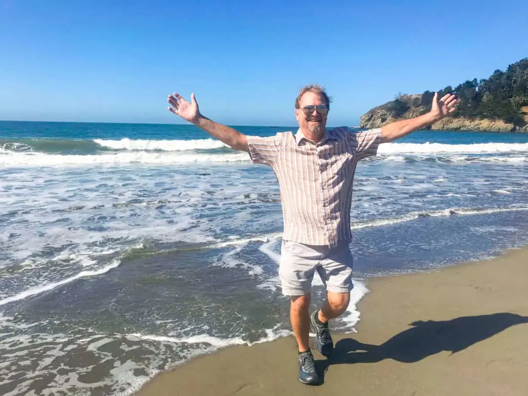 Randy Smith with arms outstretched on a beach, embodying a blessing and inspiring faith.