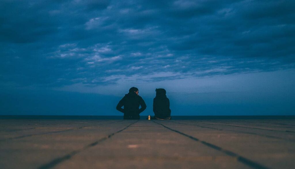 Two figures sitting and sharing faith stories authentically outdoors