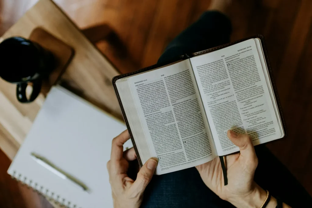 Person reading an open Bible with a notebook and coffee nearby